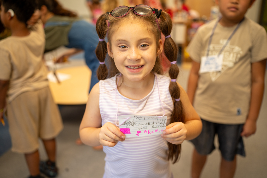 Student smiles with her badge inside the classroom. 