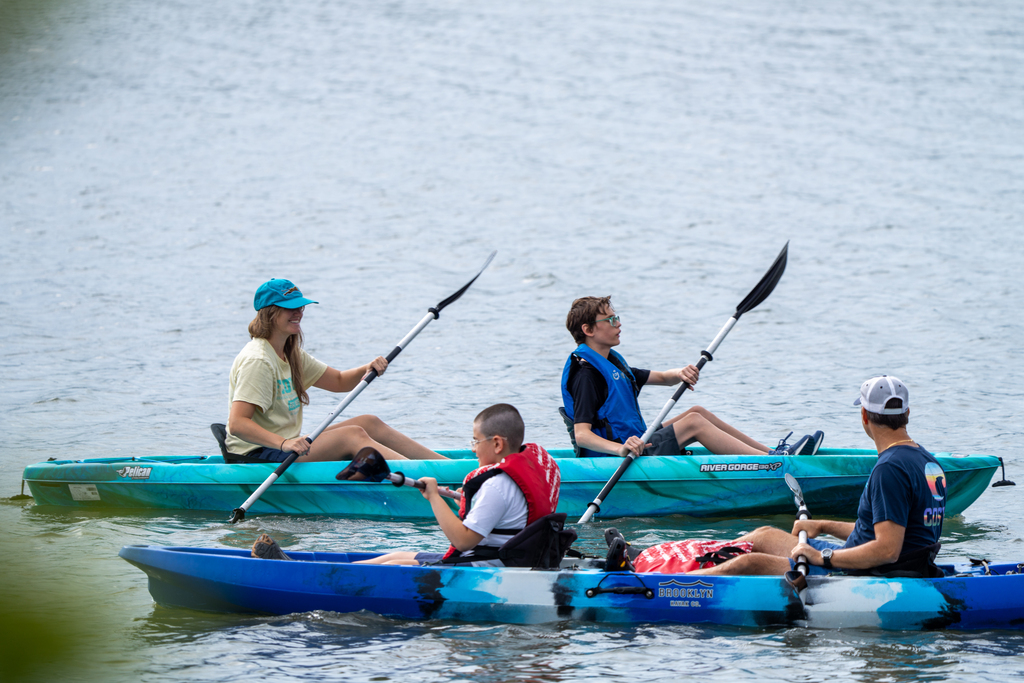Two kayaks with staff member and camper pass each other out on the water. 