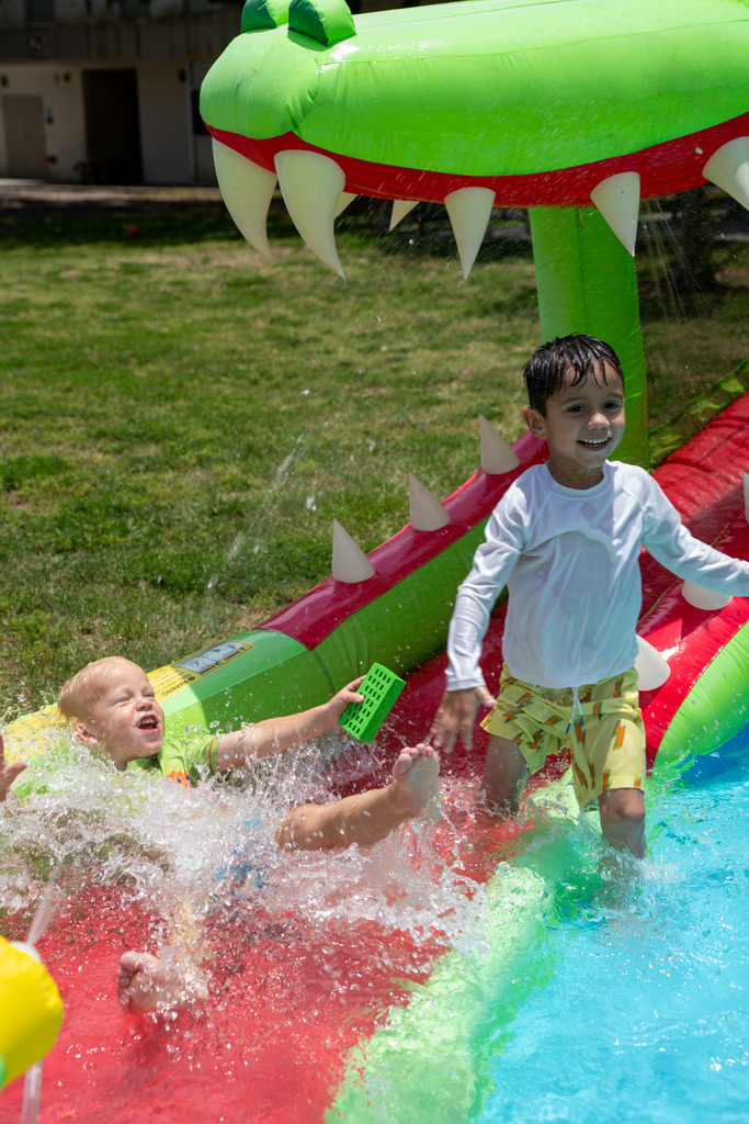 Two students play in the water slide area together outside on the grassy area of FSDB. 