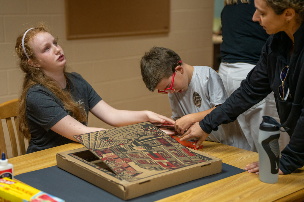 Two students and a staff member helps each other with the pizza box solar oven inside Cary White. 