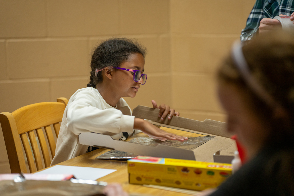 A student is adding foil to the pizza box sitting down at a table inside Cary White. 