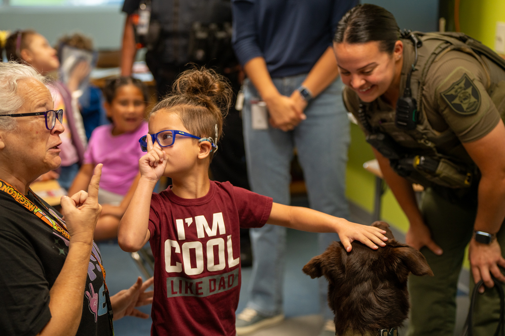 The camper tells a staff member to be quiet as he pets the dog head inside the classroom.