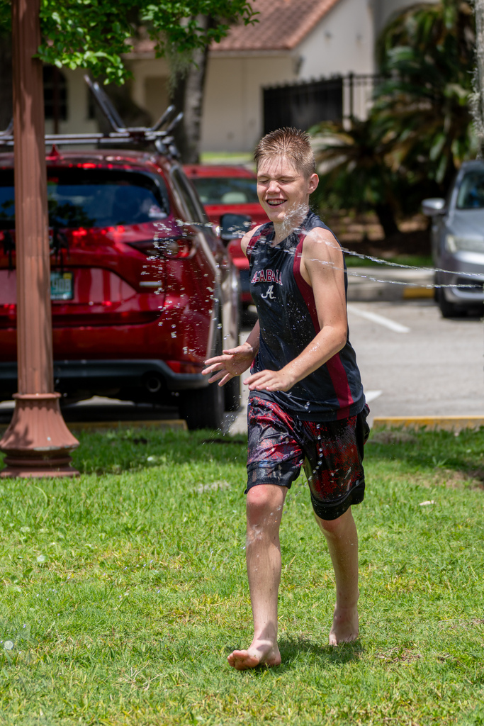 Student walks on the grass as he gets sprayed with water guns.