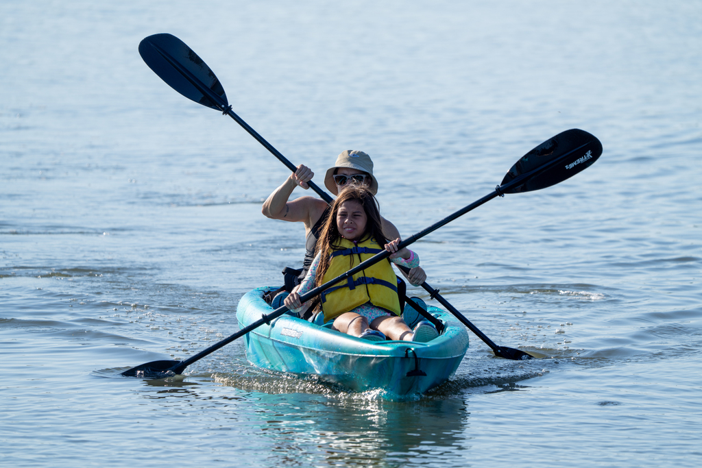 A camper and staff kayak together in a blue kayak out on the water.