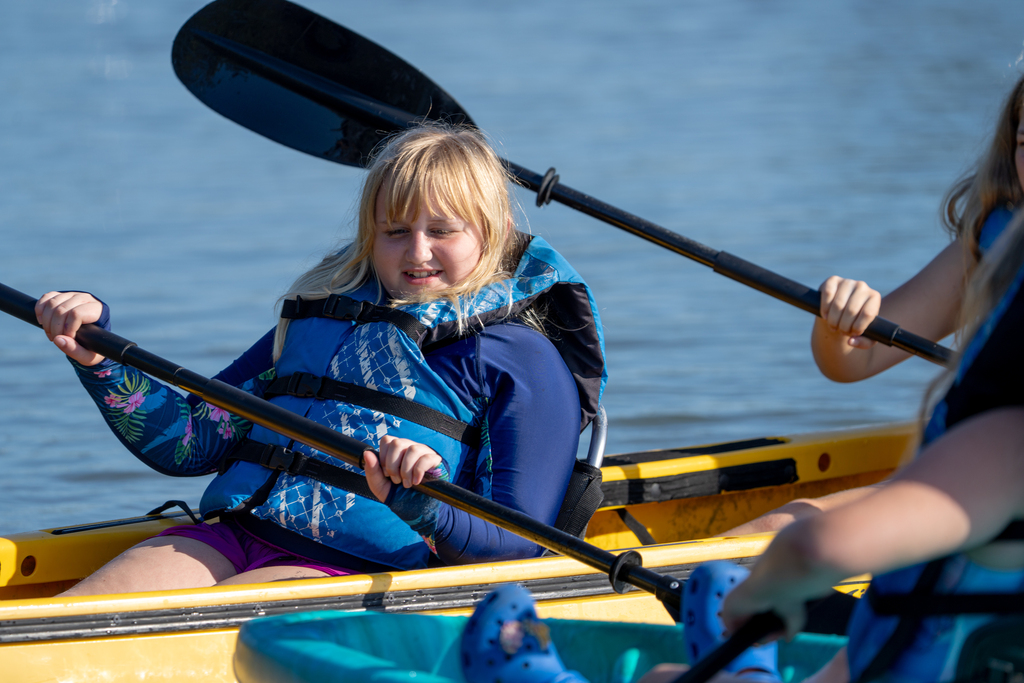 A camper smiles as she paddles on a yellow kayak out on the water. m