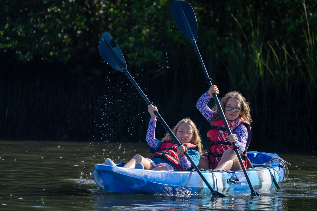 Two campers kayak together out on the water in a blue kayak.