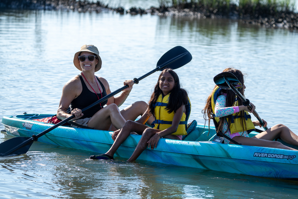 A staff member and two campers smile for a photo in a blue kayak.