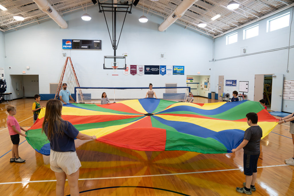 A wide shot of students and staff playing with the parachute inside the gym.