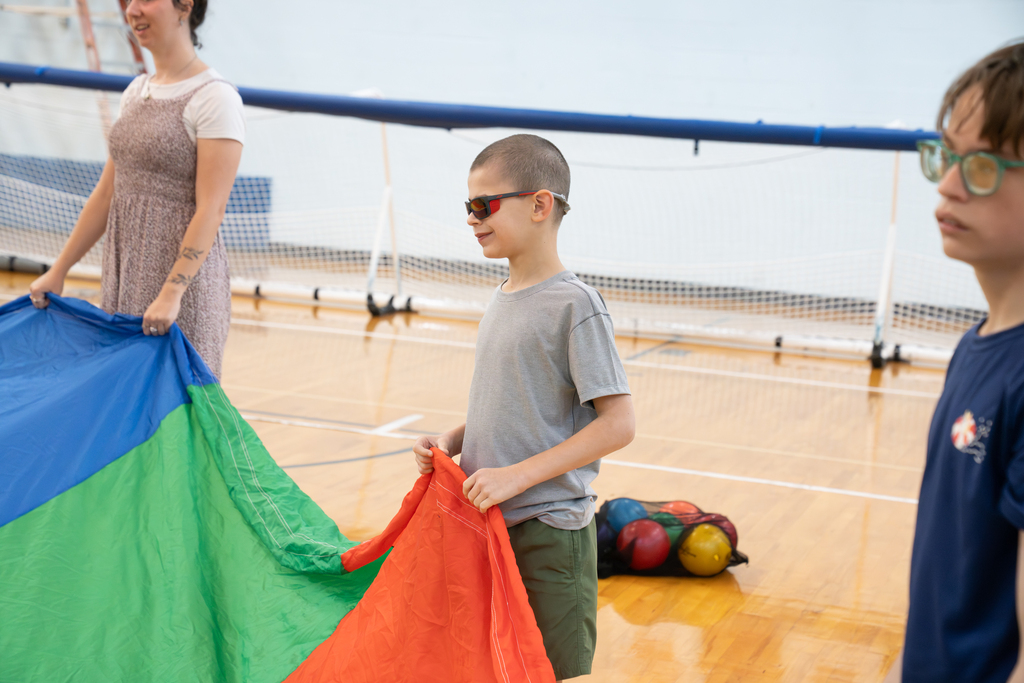A student smiling as he holds the parachute inside the gym.