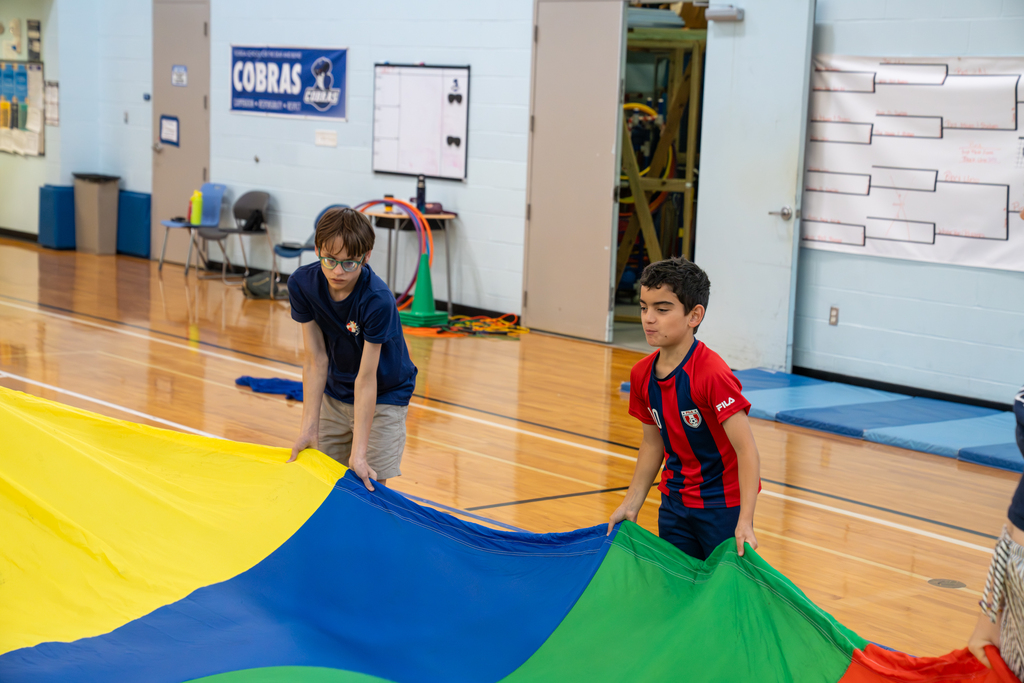 Two students holding onto the parachute inside the gym.