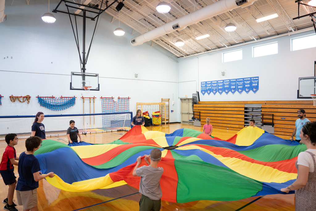 A wide shot of students and staff playing with the parachute inside the gym.