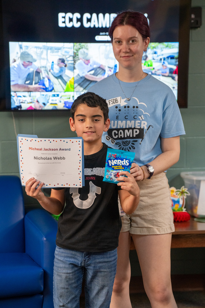 A camper smiling with a staff member holding his award and candy.