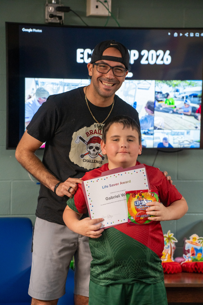 A camper smiles with a staff member holding his award and candy inside Cary white.