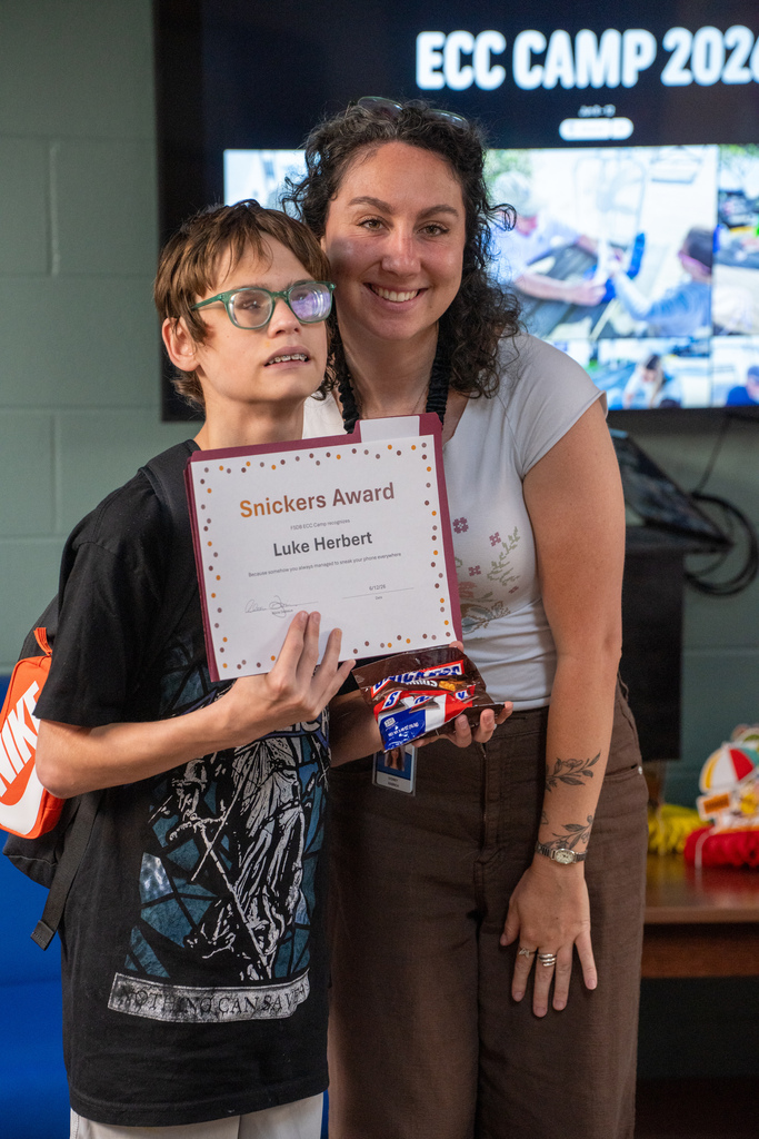 A camper smiles with a staff member holding his award and candy inside Cary White.