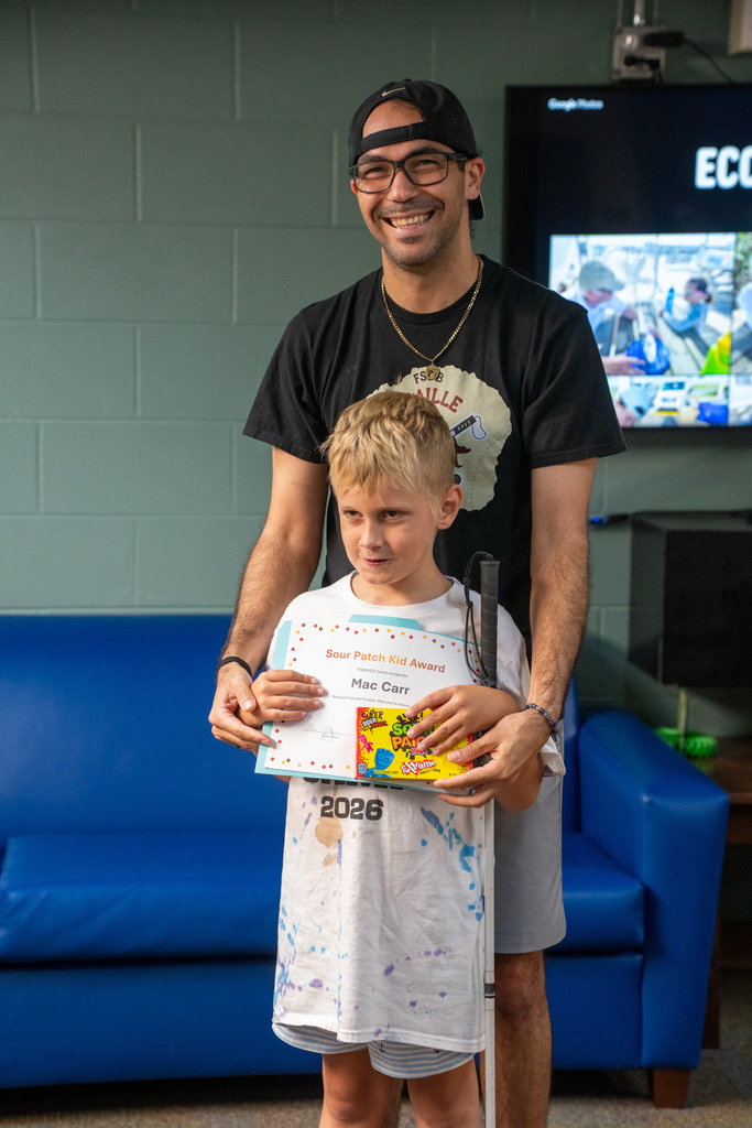 A camera smiles with a staff member holding his award and candy inside Cary White.