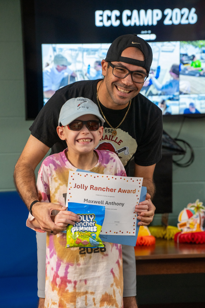 A photo of a camper with a staff member smiling with his award and candy inside Cary White.