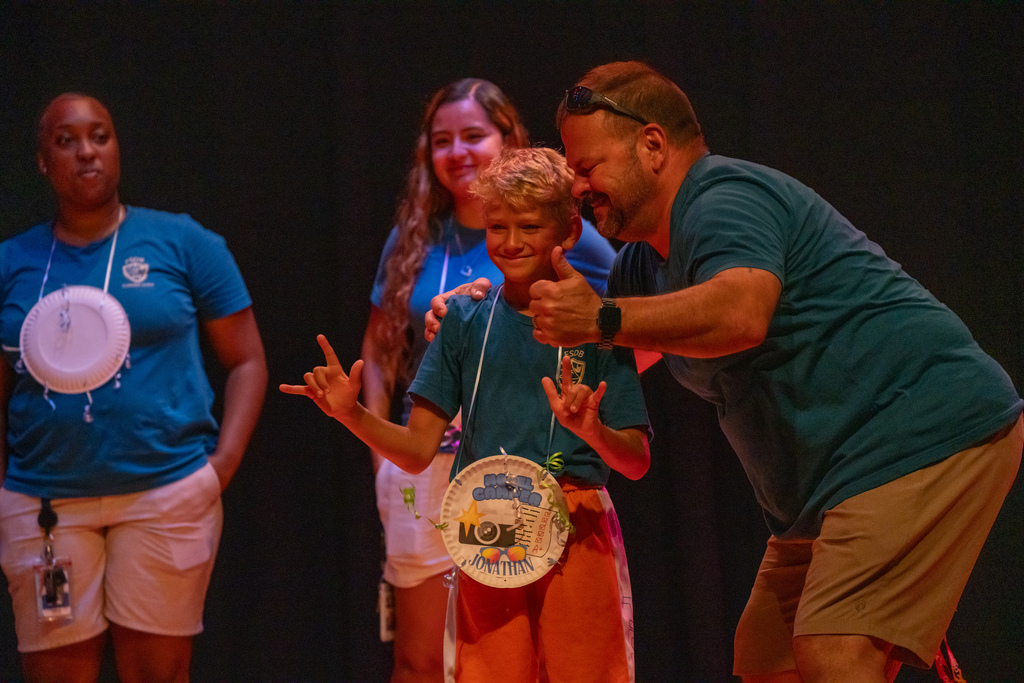 A camper smiles with his award and a staff member on stage.