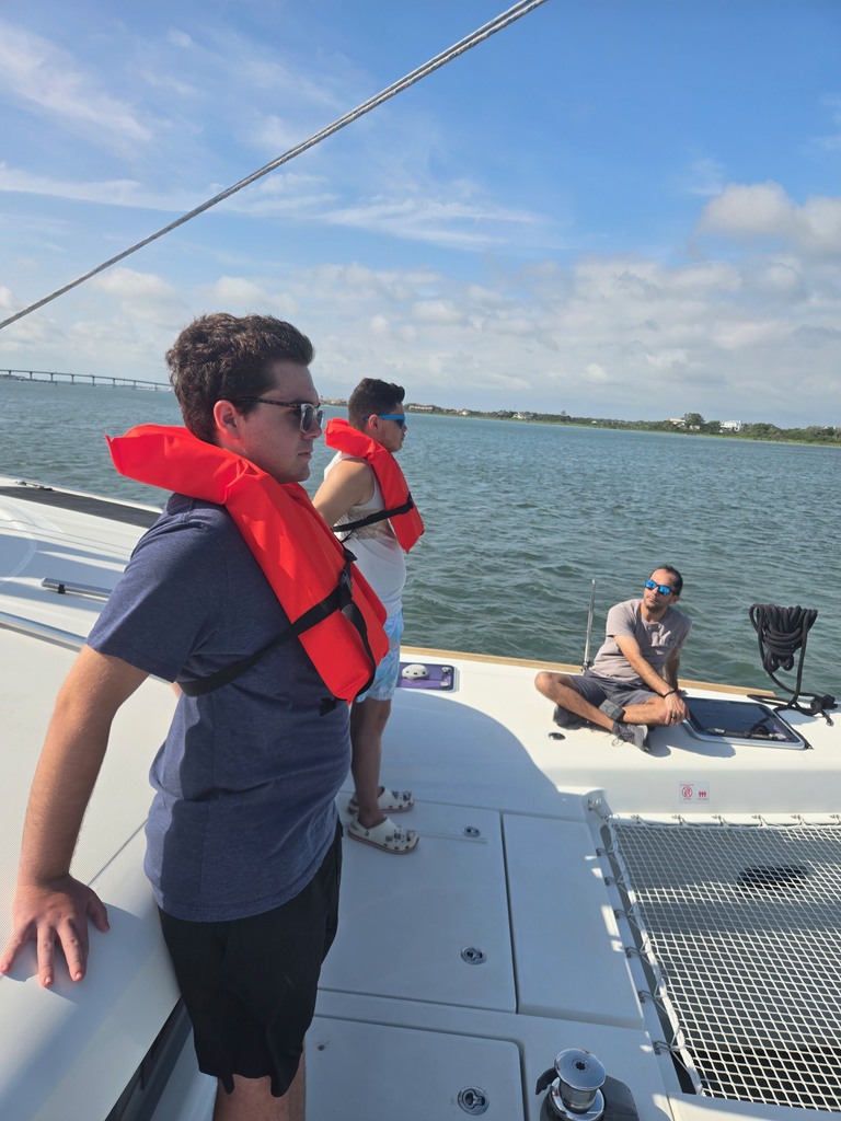 Two campers stand and wear red life guard jackets on a boat. 