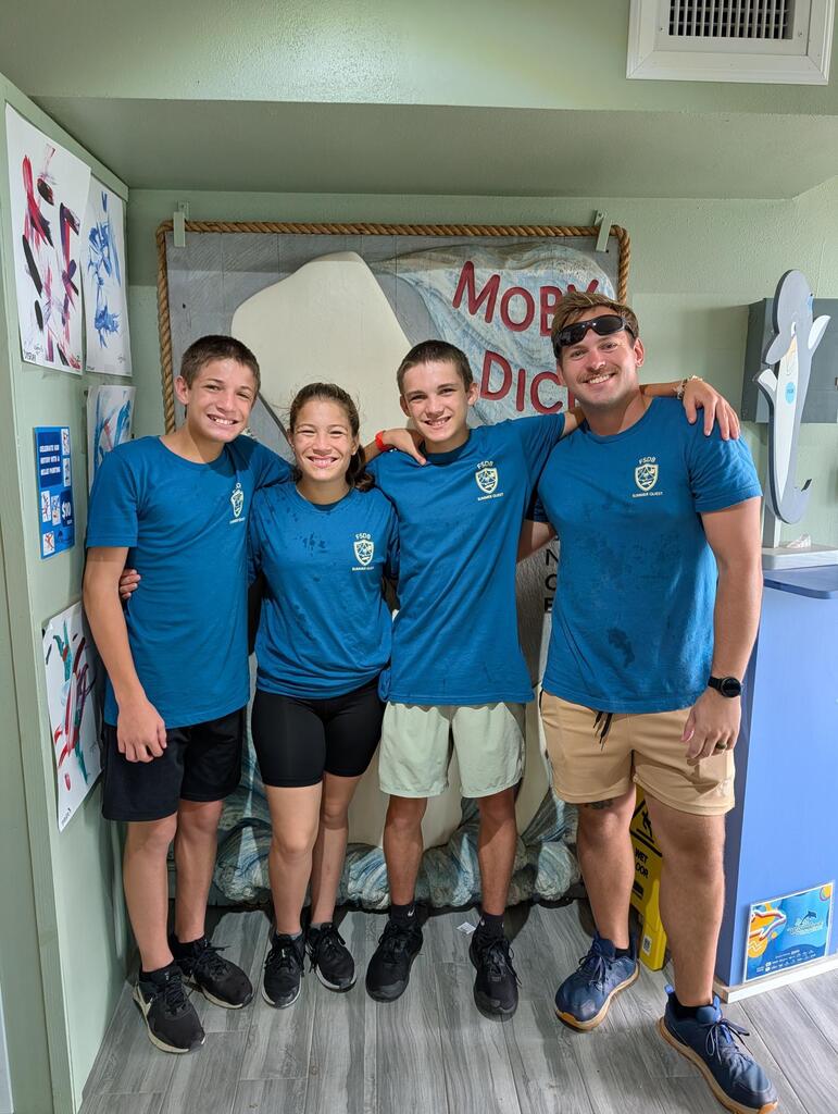 Group of students smile for a photo with a staff member inside Marine Land. 