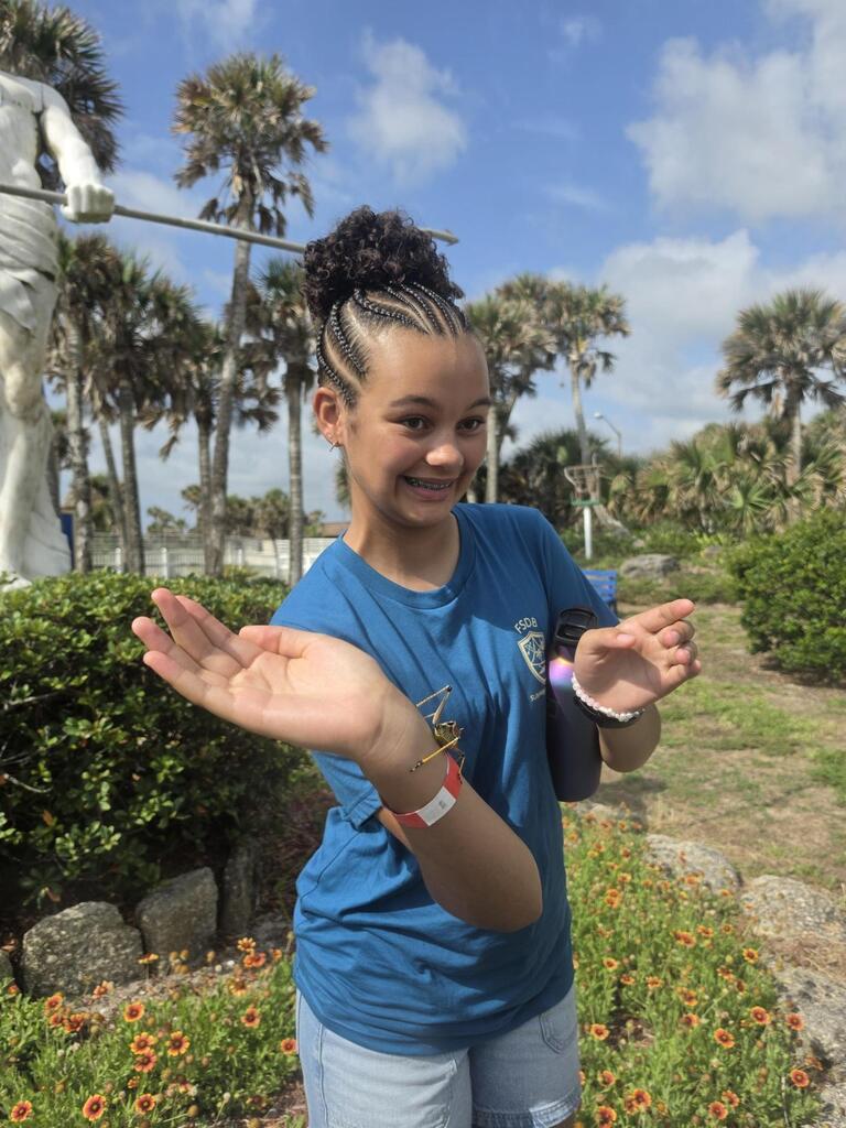 A student smiles with her hand out as a grasshopper walks on her arm outside Marineland. 