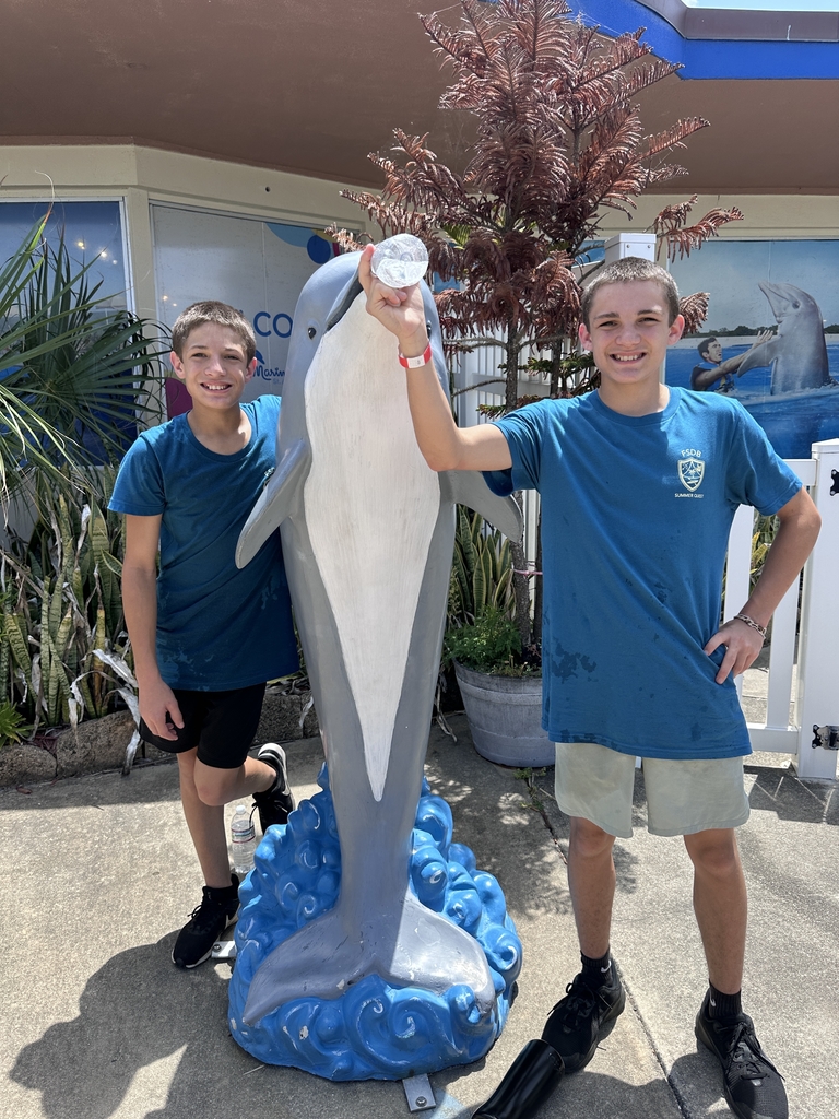 Two students smile for a photo with a dolphin statue at Marine Land. 