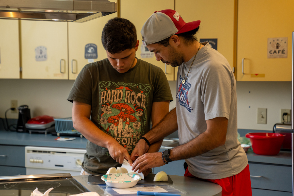 A student and staff member work on cutting onions together inside the kitchen. 