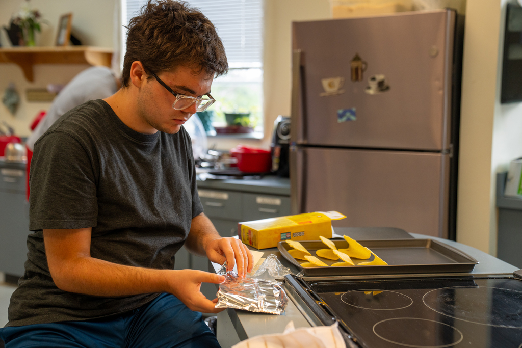 A student is getting the hard shells ready for the oven inside the kitchen. 