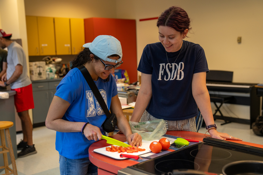 A student and staff member work on cutting the tomatoes inside the kitchen. 
