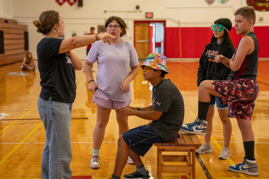 The staff member tells the campers the ideas of the skit inside the gym. 