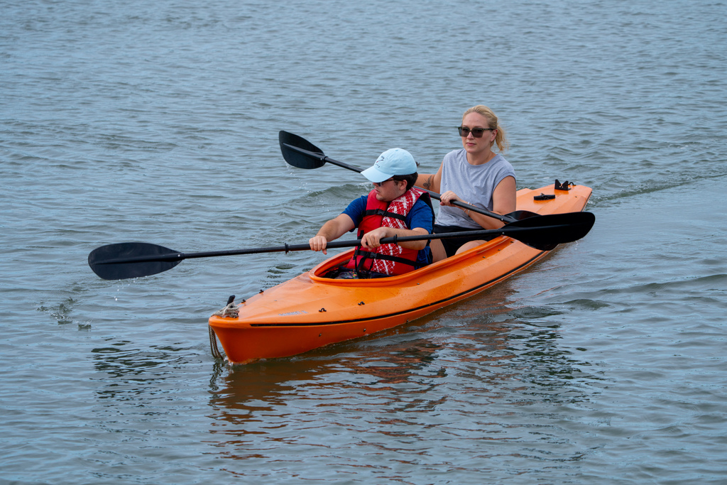 A camper  and staff member sit in the orange kayak out on the waters. 