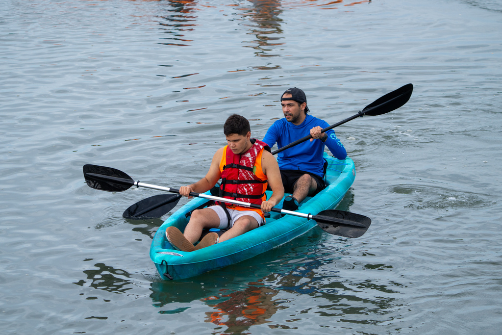 A camper and staff member sit in a blue kayak out on the waters. 