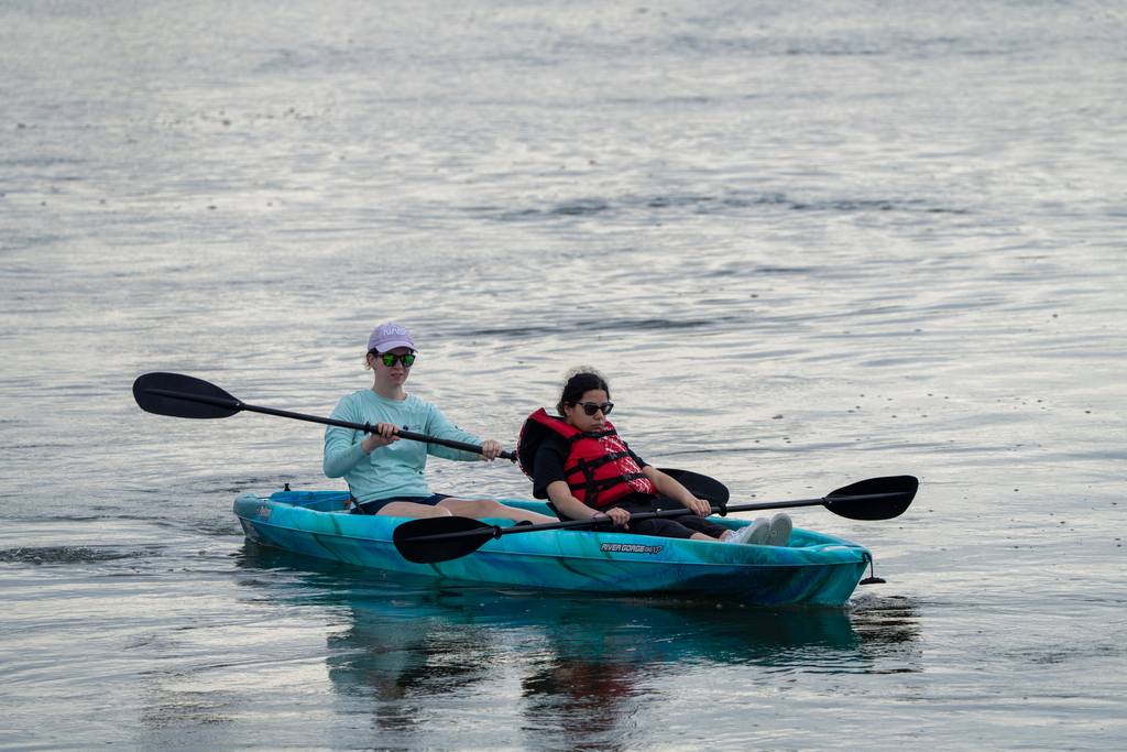 A camper and staff member sitting in a blue kayak out on the waters. 