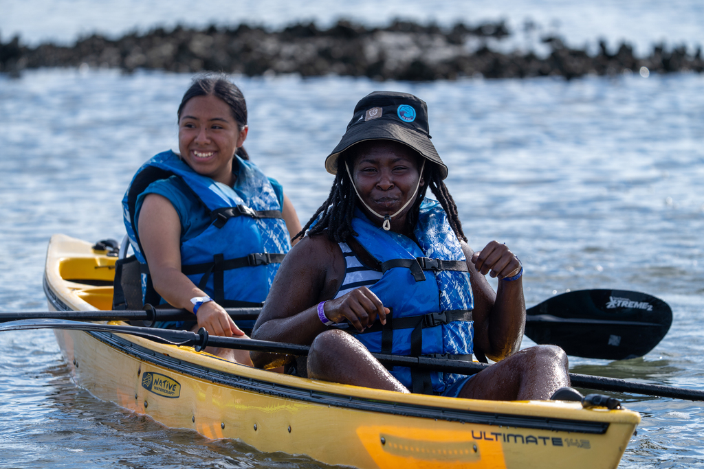 Two campers smile for a photo in a yellow kayak out on the waters. 