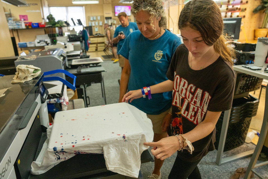 A camper and staff member learns how to print a shirt inside DB Designs. 