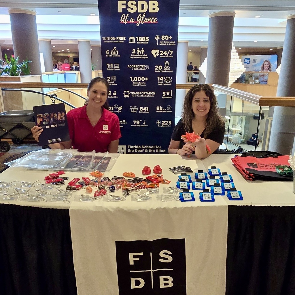 Alvina and Lenore are sitting at a booth inside the convention building. 