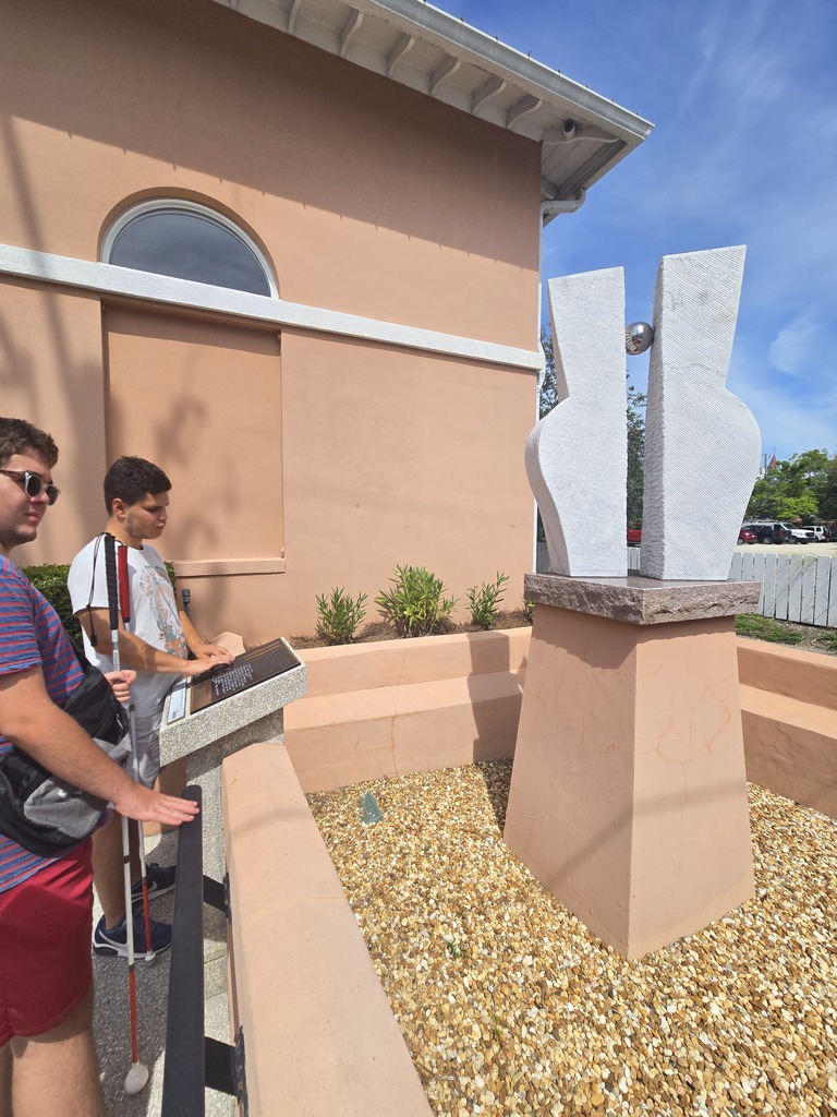 Two campers read the braille about a sculpture in downtown. 