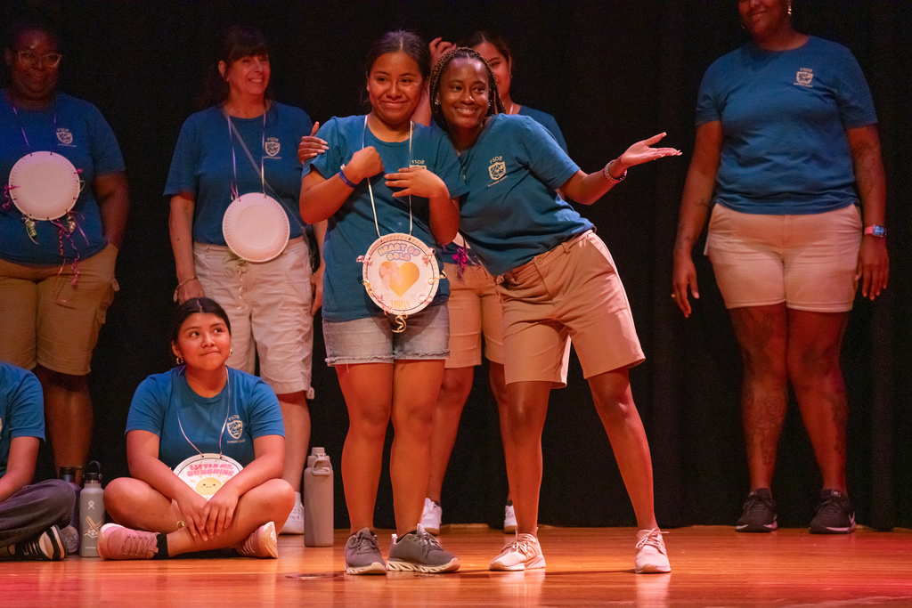 A camper smiles with a staff member who got a paper award on stage in the music building.