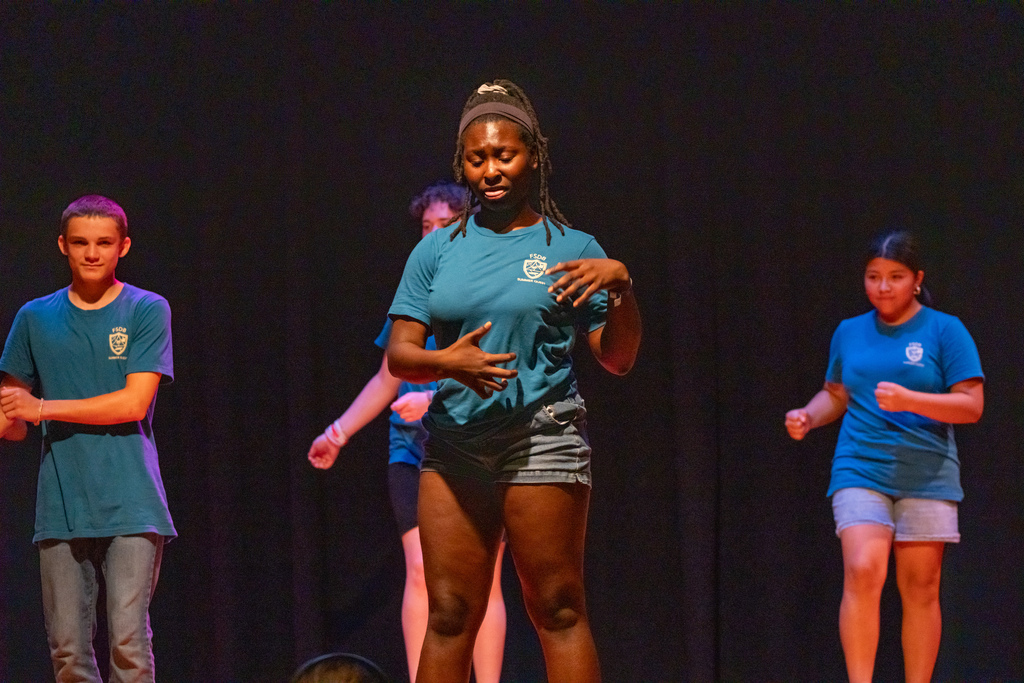 A camper signs a song on stage in the music building.
