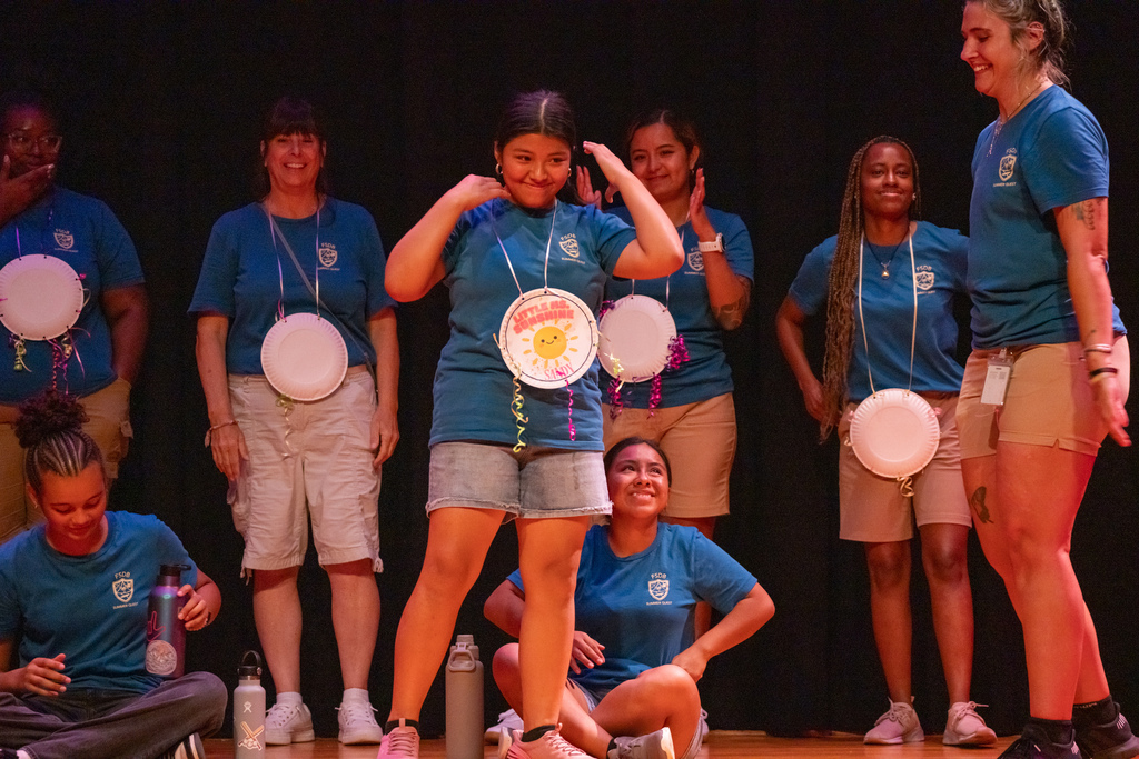 A camper smiles with her paper award on stage in Music Building.