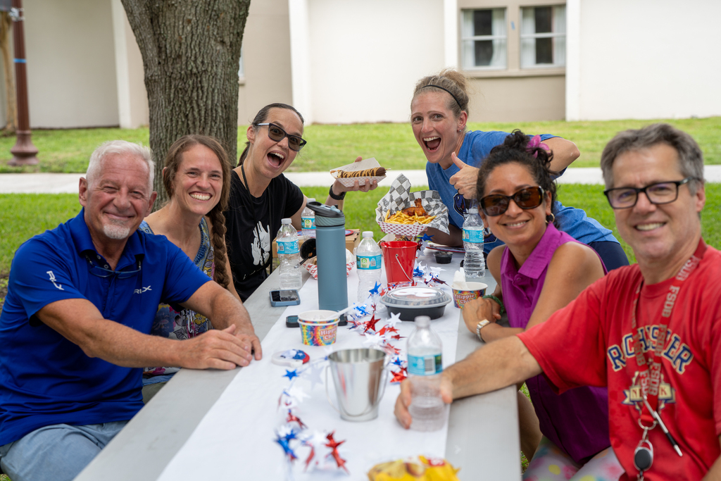 Group of staff members sit at a table smiling for their photo outside.