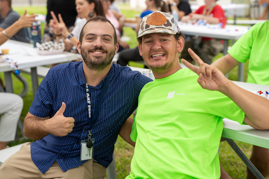 Two staff members smile for their photo at the lunch tables outside.