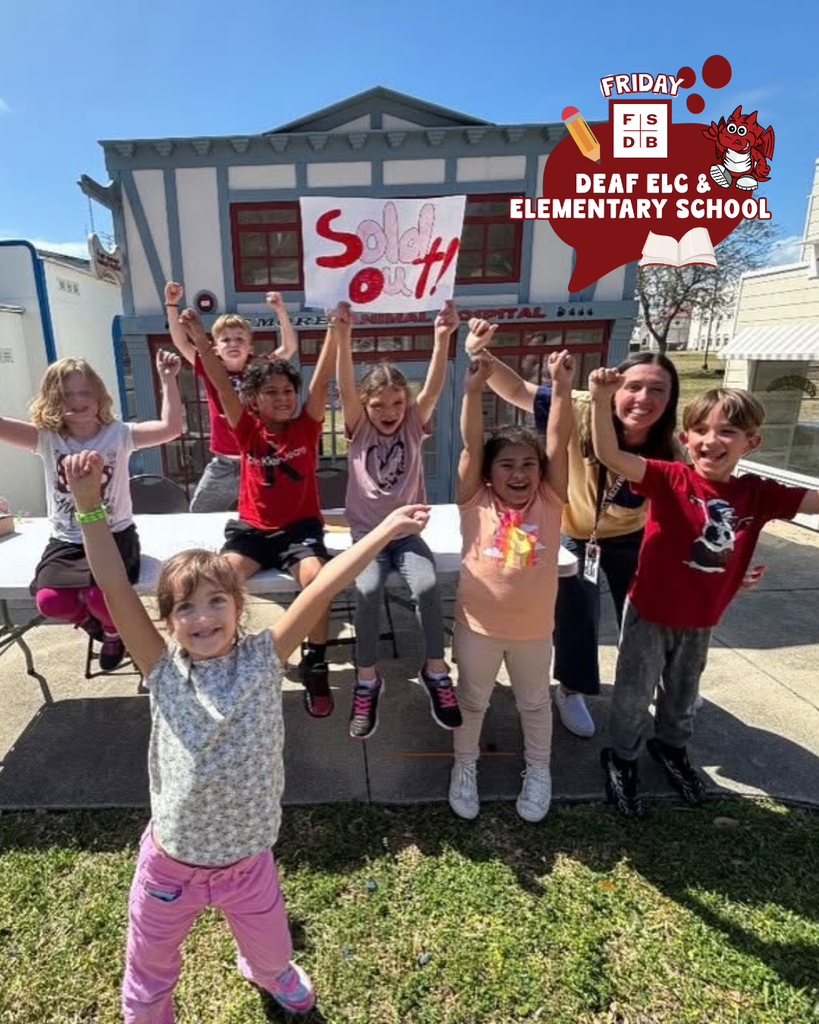Group of deaf elementary students smile with their hands in the air outside of Kids Town. 
