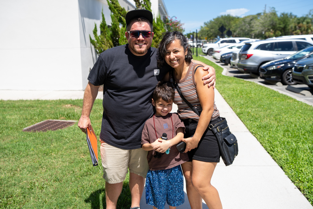 A student smiles with his parents outside.