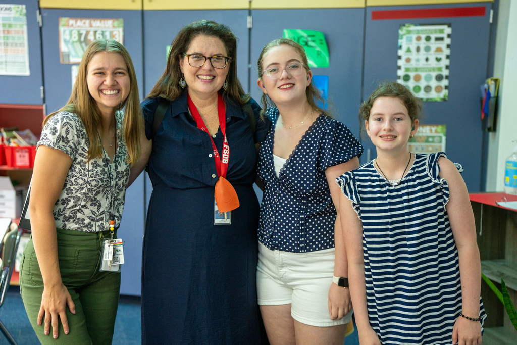 Students smile with their mother and teacher inside the classroom.