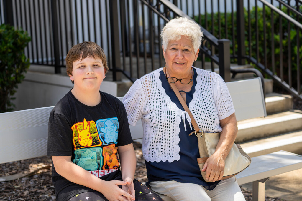 A student smiles with his family outside on a bench.