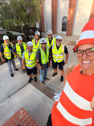 AP dressed as a bright orange traffic cone with the Safety and Facilities department behind her wearing neon safety vests and hard hats.