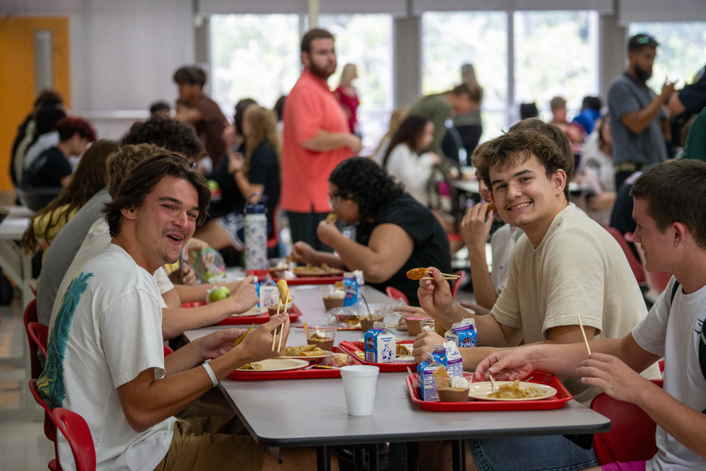 Students smile while eating their lunch inside the cafeteria.