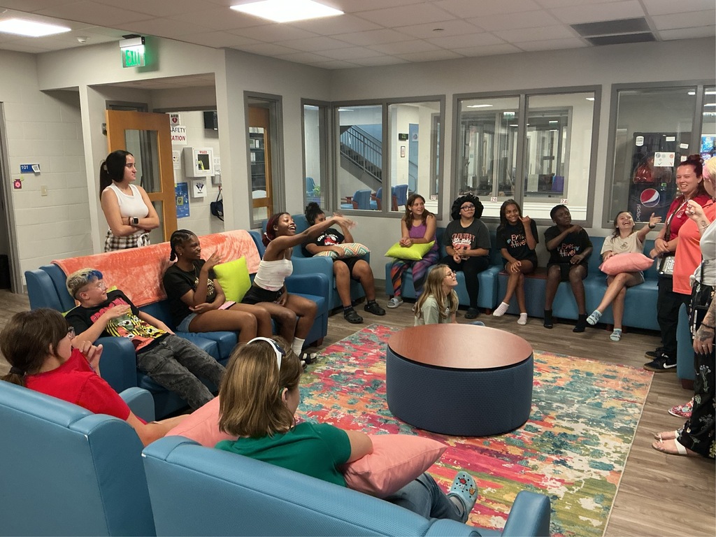 Group of students sit on the couch gathering around looking at their instructors.