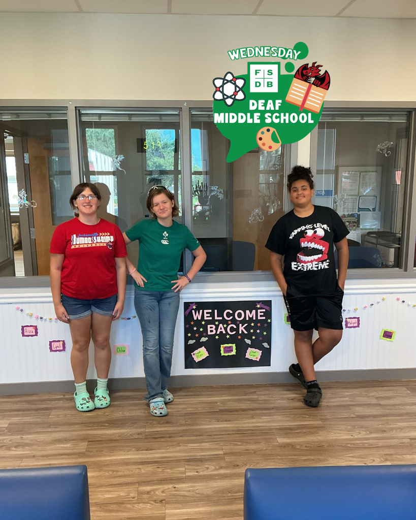 Three students are smiling by the window with a "Welcome Back" black poster in between them.