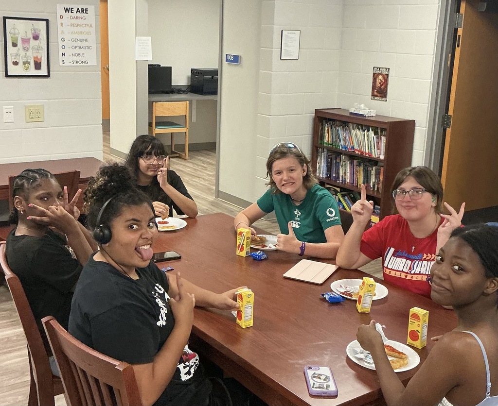 Students sit at a table smiling for their photo inside Gregg Hall.